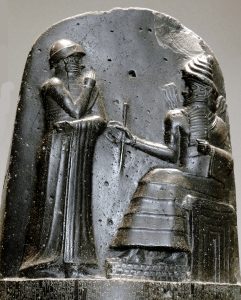 Hammurabi (standing), depicted as receiving his royal insignia from Shamash (or possibly Marduk). Hammurabi holds his hands over his mouth as a sign of prayer[1] (relief on the upper part of the stele of Hammurabi's code of laws). Photo by Mbzt, WIkipedia Commons.