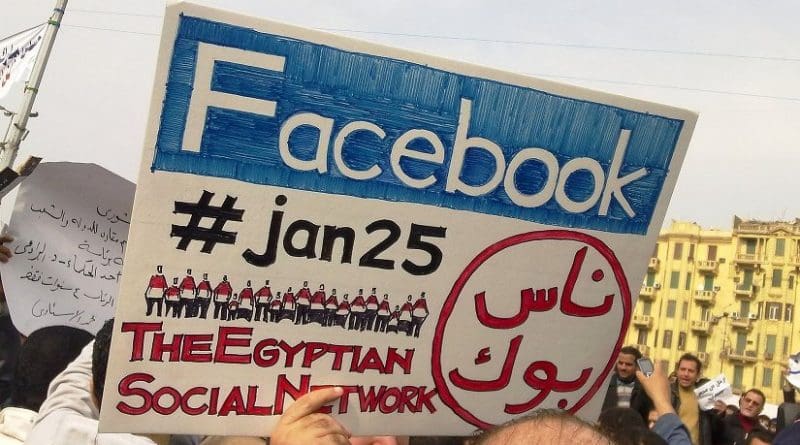 A man during the 2011 Egyptian protests carrying a card saying "Facebook,#jan25, The Egyptian Social Network". Photo by Essam Sharaf, Wikipedia Commons.