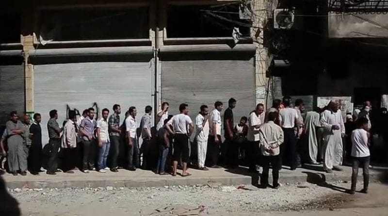 Aleppians waiting in a bread line during the Syrian civil war. File photo Voice of America News, Scott Bobb. Wikipedia Commons.