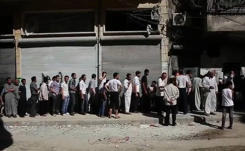 Aleppians waiting in a bread line during the Syrian civil war. File photo Voice of America News, Scott Bobb. Wikipedia Commons.