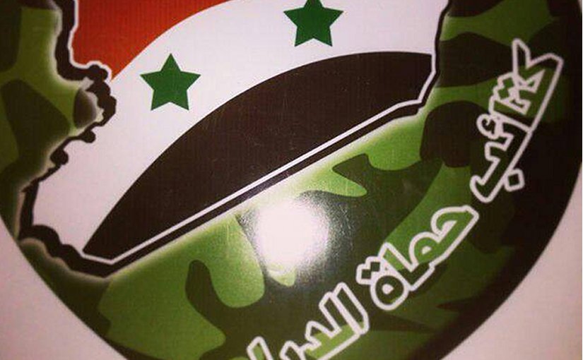 Emblem of Kata’ib Humat al-Diyar, featuring Syria as the main part of the emblem and the group’s name beneath it.
