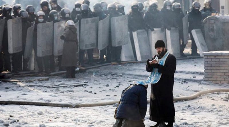 A man kneels before an Orthodox priest in an area separating police and anti-government forces in Ukraine.