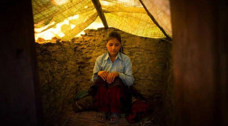 Wearing her school uniform, Jaukala, 14, poses for a photo in the family's chaupadi shelter, a squat shed measuring approximately 1 meter by 2 meters, in Rima village, Achham, Nepal. A tarp serves as a temporary roof to this structure, still under construction. Jaukala must sleep here while she has her period. Courtesy of Allison Shelley