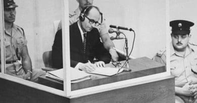 Defendant Adolf Eichmann takes notes during his trial in Jerusalem. The glass booth in which Eichmann sat was erected to protect him from assassination. (Photo credit: Israeli Government)