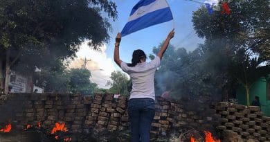 A woman stands near a burning barricade holding the national flag of Nicaragua. Photo Credit: VOA