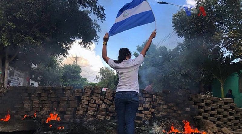 A woman stands near a burning barricade holding the national flag of Nicaragua. Photo Credit: VOA