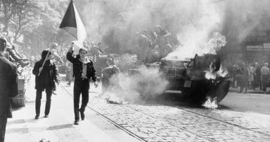 During the Soviet invasion of Czechoslovakia, Czechoslovaks carry their national flag past a burning tank in Prague. Photo Credit: CIA, Wikimedia Commons.