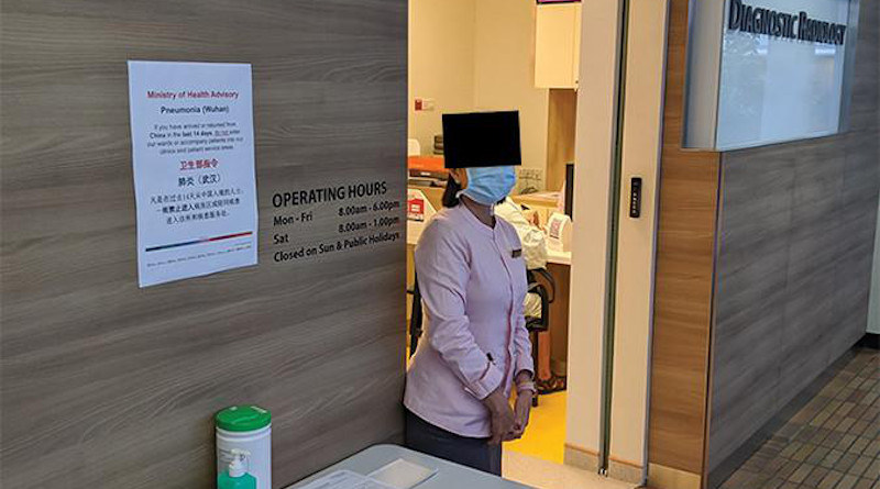 Screening station setup at radiology department entrance in early phase of outbreak, including staff member wearing mask. These smaller department-level screening stations were subsequently replaced by larger screening facilities at entrances to each building. (Obscuring of facial features has been applied for privacy reasons for publication.) CREDIT American Journal of Roentgenology (AJR)