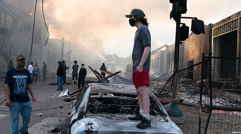 A man stands on a burned out car in Minneapolis, Minnesota during George Floyd protests. Photo Credit: Lorie Shaull, Wikipedia Commons.