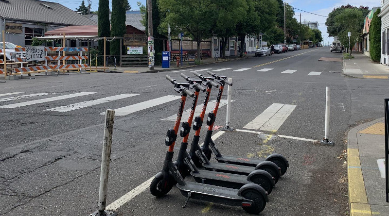 Several shared e-scooters, available for rental through a mobile app, occupy a curbside parking space that would fit a single automobile. CREDIT: Photo by Cait McCusker