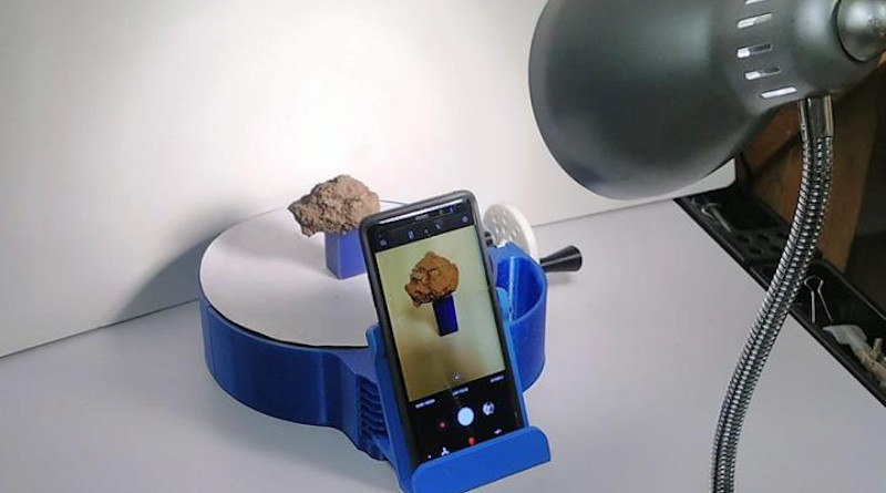Experimental set up showing soil sample on a 3D-printed turntable with cell phone. A light provides consistent illumination while a white background and white turntable top reduce background influence. The soil sample is rotated on the turn table while taking an image every one fourth rotation. CREDIT: Colby Brungard