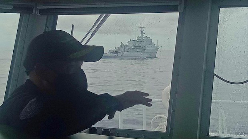 A Philippine Coast Guard officer aboard the BRP Cabra observes a Chinese Navy warship near the Marie Louise Bank in the South China Sea, July 13, 2021. Courtesy Philippine Coast Guard