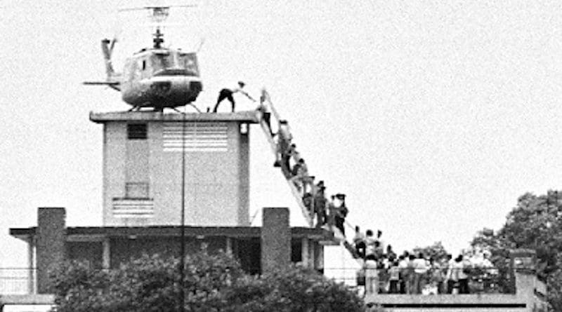 A member of the CIA helps evacuees up a ladder onto an Air America helicopter on the roof of 22 Gia Long Street April 29, 1975, shortly before Saigon fell to advancing North Vietnamese troops. Photo Credit: Hubert van Es, Wikipedia Commons