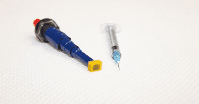 Georgia Tech’s ePatch, containing a microneedle electrode array (yellow) affixed to an electroporation pulser made from a BBQ lighter (blue), is shown next to a needle and syringe. CREDIT: Candler Hobbs, Georgia Tech