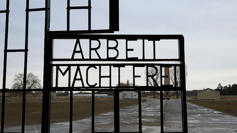 Photo caption: the gate at Sachsenhausen concentration camp, with the barren “parade ground” visible. Credit: Creative Commons image