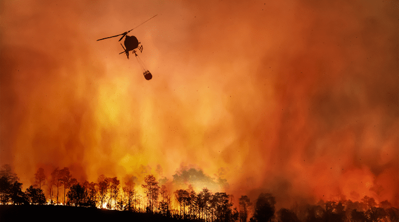 A raging wildfire in forested area with responsing helicopter in the sky CREDIT: IOP Publishing