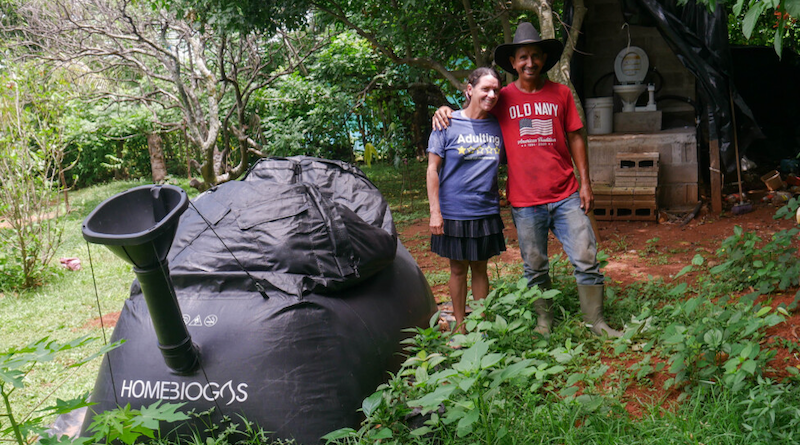 Marisol and Misael Menjívar pose next to the biodigester installed in March in the backyard of their home in El Corozal, a rural settlement located near Suchitoto in central El Salvador. With a biotoilet and stove, the couple produces biogas for cooking from feces, which saves them money. The biotoilet can be seen in the background. CREDIT: Edgardo Ayala / IPS