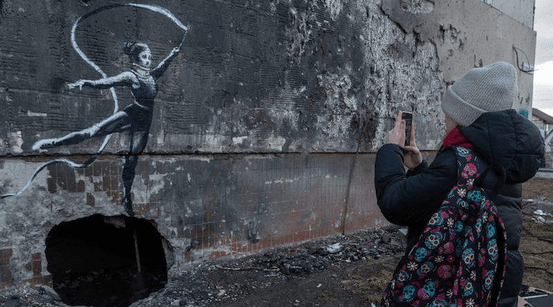 A teenager takes a photograph of a work by British street artist Banksy in the spring of 2023 in Irpin, Ukraine. Photo Credit: © UNICEF/Filippov