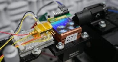 NIST researchers test a chip for converting light into microwave signals. Pictured is the chip, which is the fluorescent panel that looks like two tiny vinyl records. The gold box to the left of the chip is the semiconductor laser that emits light to the chip. CREDIT: K. Palubicki/NIST
