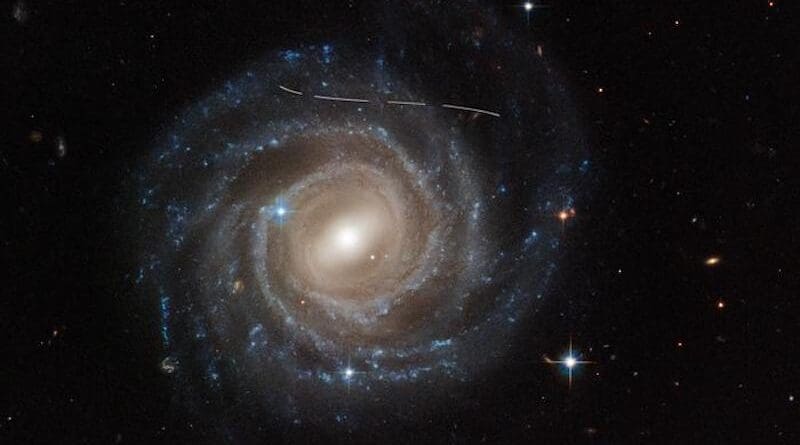 This Hubble Space Telescope image of the barred spiral galaxy UGC 12158 looks like someone took a white marking pen to it. In reality it is a combination of time exposures of a foreground asteroid moving through Hubble's field-of-view, photobombing the observation of the galaxy. Several exposures of the galaxy were taken, what is evidence in the dashed pattern. The asteroid appears as a curved trail due to parallax: because Hubble is not stationary, but orbiting Earth, and this gives the illusion that the faint asteroid is swimming along a curved trajectory. The uncharted asteroid is in inside the asteroid belt in our solar system, and hence is 10 trillion times closer to Hubble than the background galaxy. Rather than a nuisance, this type of data are useful to astronomers for doing a census of the asteroid population in our solar system. CREDIT NASA, ESA, Pablo García Martín (UAM); Image Processing: Joseph DePasquale (STScI); Acknowledgment: Alex Filippenko (UC Berkeley)