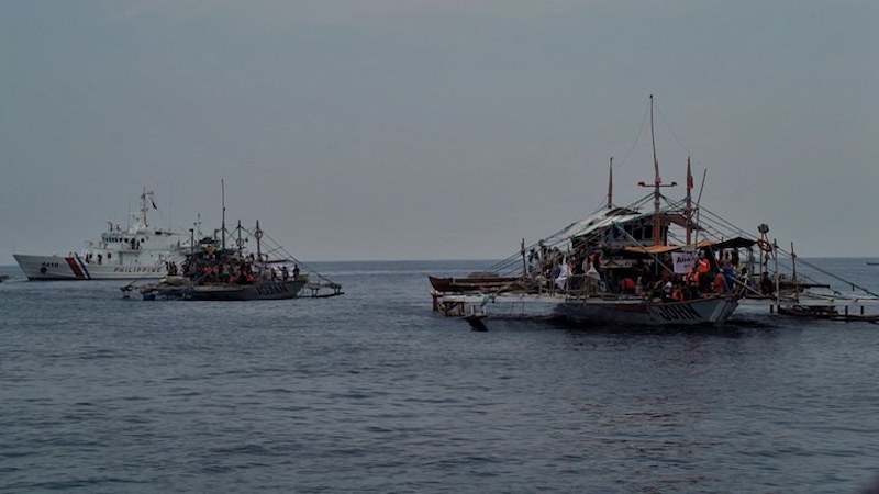 A Philippine Coast Guard ship is seen in the background as boats belonging to a civilian convoy sail toward Scarborough Shoal in the South China Sea, May 15, 2024. [Jojo Riñoza/BenarNews]