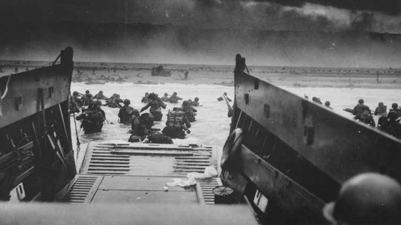 U.S. Army soldiers disembark a landing craft under heavy fire off the coast of Normandy, France, June 6, 1944. Photo Credit: National Archives